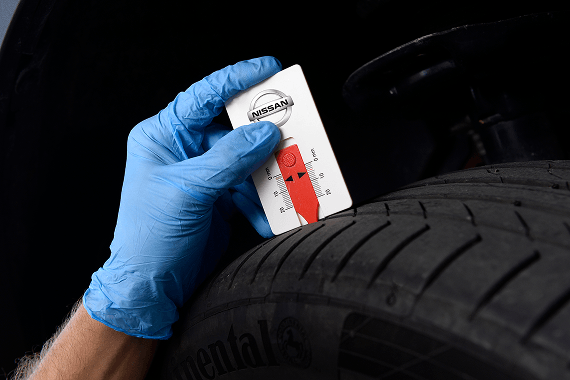 Eine Hand mit blauem Schutzhandschuh misst das Reifenprofil mit einem Nissan-Reifenprofiltiefenmesser.
